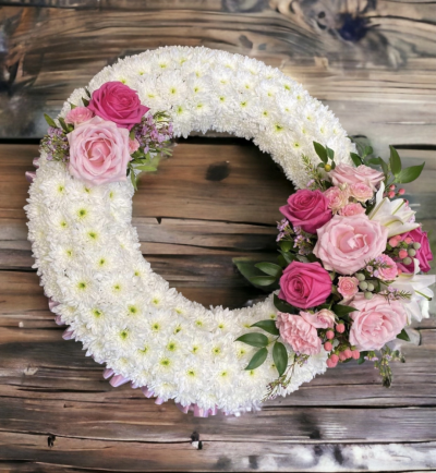 Pink Massed wreath - This beautiful funeral tribute is perfectly edged with pleated ribbon, the base is made up of chrysanthemums and a cluster of season flowers to make this massed wreath stand out. It is arranged on a wet floral foam frame. Different colours can be requested in the notes including the edged ribbon. perfect for a funeral, memorial or grave.